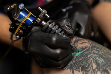 Fototapeta na wymiar Close up of a tattoo artist's hand with black glove and his tattoo machine. Body art concept