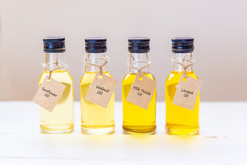 Four types of unrefined oil in small bottles, with signatures on tags on a light background. Sunflower, linseed, milk thistle oil and walnut oil. Healthy eating conceptual
