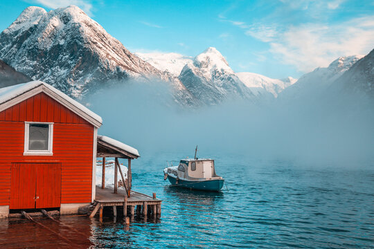 Fishing boat going out into the fog in fjord with snowy mountains in the background