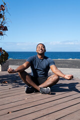 Fototapeta na wymiar Happy man meditating in lotus position while doing yoga on beach