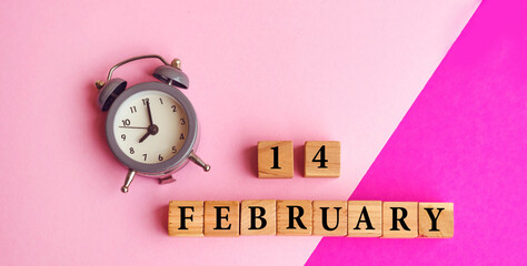 Pink Greeting Card with Wooden Calendar and alarm clock . Wooden cubes with 14 February text 