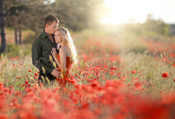 a beautiful young guy and a girl in a red dress hug and have fun in a field with poppies..