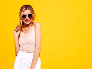 Young beautiful smiling female in trendy summer clothes. Sexy carefree woman posing near yellow in studio. Positive model having fun. Cheerful and happy. In sunglasses