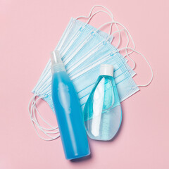 Blue medical face masks, sanitizer spray and a hand antiseptic gel on pink background for protection against Viruses, Flu, Coronavirus, COVID-19. Flat lay.