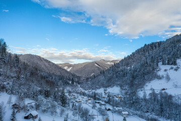 Mountains landscape. Winter Carpathian forest with spruces. Small village in the foreground. Ukraine.