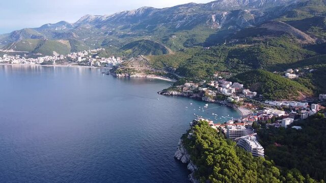 Bird's eye view of holiday town by the sea. Town is located at the foot of the mountain with green forests.