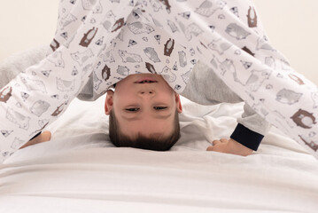 Child boy standing upside down and showing tongue on his bed at the morning. Morning exercises. Relaxing at home concept. Happy childhood