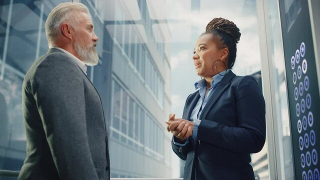 Middle Aged Businessman Talking with International Investment Partner while Riding Glass Elevator to Office in a Modern Business Center. Corporate Associates Shake Hands on Successful Deal.