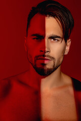 Young, athletic and strong guy. He has a naked torso on a red background. A ray of light falls on one eye. The guy has a very serious look