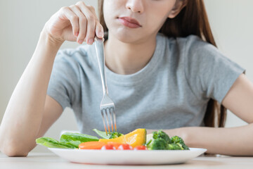 Diet in bored face, unhappy beautiful asian young woman, girl on dieting, holding fork in salad plate, dislike or tired with eat fresh vegetables. Nutrition of clean, healthy food good taste. - obrazy, fototapety, plakaty