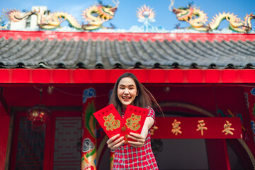 Beautiful Asian woman wearing a traditional red cheongsam on Chinese New Year.Hand holding red envelope or Ang pao with Chinese character means happiness or good fortune.