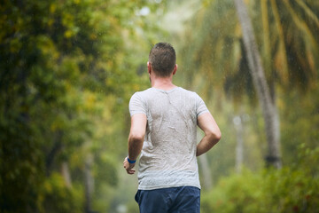 Rear view of runner in heavy rain. Drenched young man runing in nature.