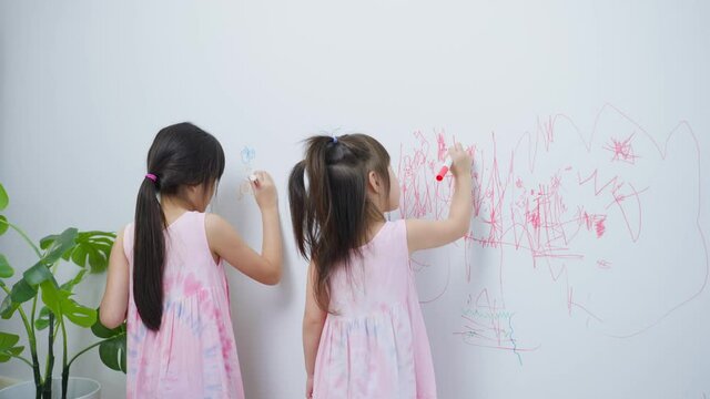 Asian young sibling kid girl enjoy paint on white wall in living room.	