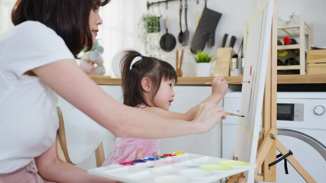 Asian young happy kid daughter coloring on painting board with mother.	