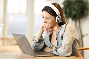 Happy woman watching media on laptop wearing headphones