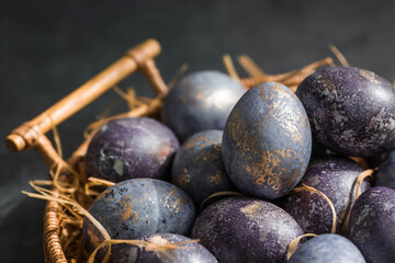Easter card with a copy of the place for the text. Purple, blue and golden eggs in a basket on a dark background. The purple hue trend of 2022 is very peri. Natural dye karkade tea. Top view