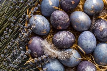 Easter card with a copy of the place for the text. Purple, blue and golden eggs with lavender on a dark background. The purple hue trend of 2022 is very relevant. Natural dye karkade tea. Top view.