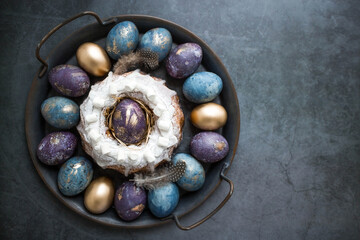 Easter card with a copy of the place for the text. Purple, blue and golden eggs with a cake on a dark background. The purple hue trend of 2022 is very peri. Natural dye karkade tea. Top view.