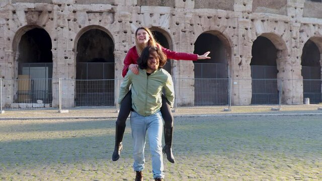 Young couple traveling to Rome. The beautiful couple is having fun in front of the Colosseum. The man picks up his girlfriend.