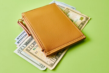 Orange leather wallet lies on dollar bills on a green table.