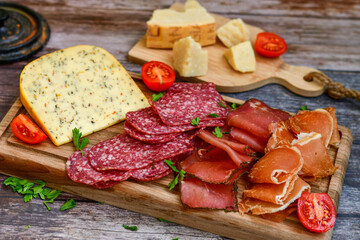 Italian  dried thinly sliced   artisan  pork salami Milano ,  mediterranean parmesan cheese, tomatoes   and fresh basil on wooden background .Rustic  home made italian snack.