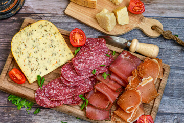 Italian  dried thinly sliced   artisan  pork Salami Milano ,  mediterranean Parmesan cheese, tomatoes   and fresh basil on wooden background .Rustic  home made Italian snack.