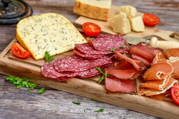 Italian  dried thinly sliced   artisan  pork Salami Milano ,  mediterranean Parmesan cheese, tomatoes   and fresh basil on wooden background .Rustic  home made Italian snack.