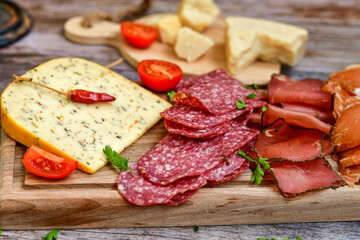 Italian  dried thinly sliced   artisan  pork Salami Milano ,  mediterranean Parmesan cheese, tomatoes   and fresh basil on wooden background .Rustic  home made Italian snack.