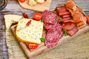 Italian  dried thinly sliced   artisan  pork Salami Milano ,  mediterranean Parmesan cheese, tomatoes   and fresh basil on wooden background .Rustic  home made Italian snack.
