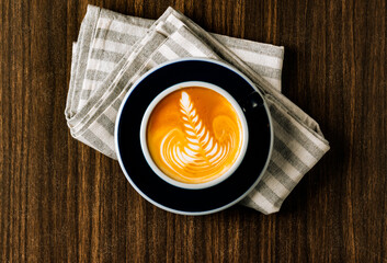 Hot Caramel latte Macchiato coffee with coffee beans in a black mug top view in dark wooden table background.