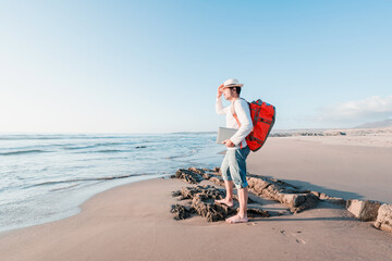 digital nomad with a backpack and laptop on the beach staring at sunset 