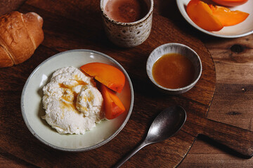 Homemade ricotta cheese or cheese curd served with fresh persimmon and honey and croissante on wooden background. Healthy breakfast. Haze effect. Selective focus