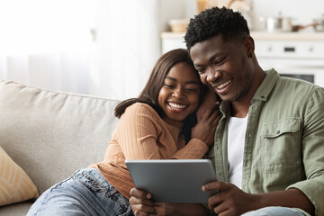 Happy black lovers using digital tablet together, home interior