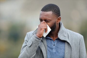 Sick guy with black skin blowing on tissue in winter