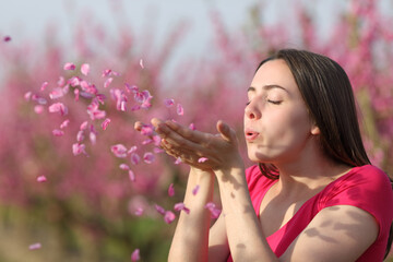 Woman blowing flower petals to the air in a field