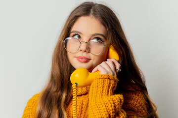Beautiful girl in glasses and yellow sweater with yellow dial phone