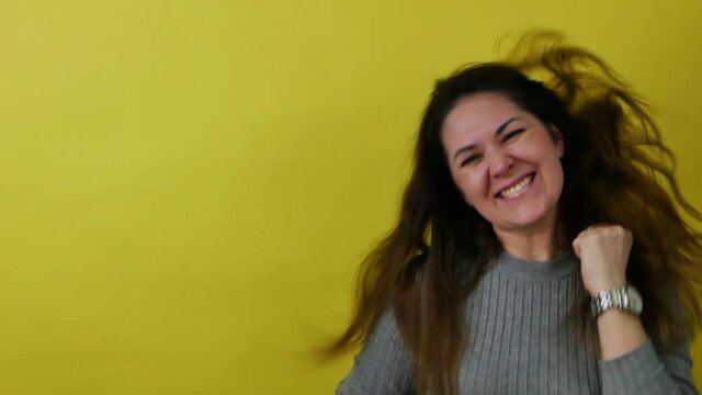 A woman in gray clothes on a yellow background jumps and dances with great joy.