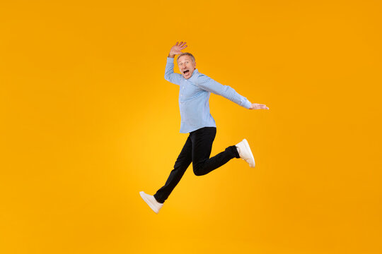 Excited mature man jumping up at orange studio