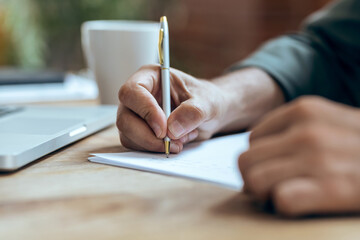 Hand of mature business man writing some notes in notebook while working with laptop  in the office.