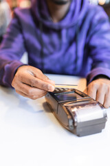 Crop unrecognizable African American male client using bank card for contactless payment with NFC technology via wireless terminal in cafe