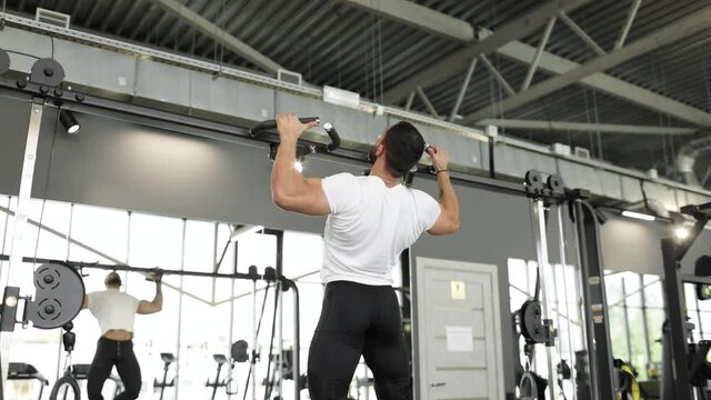 A strong caucasian man dressed in workout clothes does reps on the pull-down equipment in a gym. Back view. The concept of the sports industry and active lifestyle.