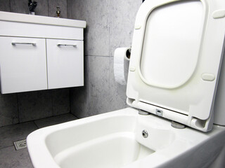    White toilet bowl in the bathroom. A gray wall with ceramic tiles in the background. Gray floor ceramic tile.       