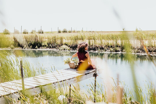 Black woman sits on dock while gazing off to the side