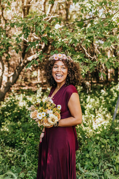 Smiling female stands in wooded area holding flower bouquet
