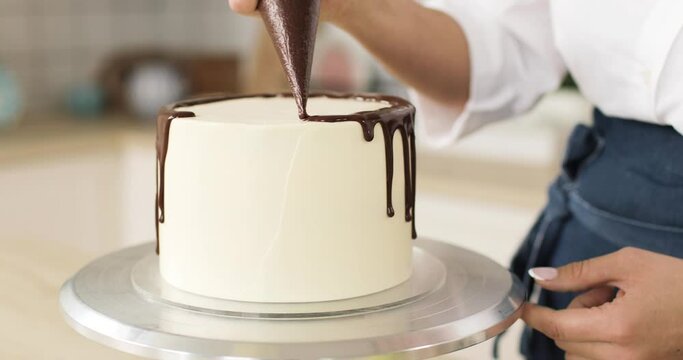 White tasty cake decorated by pastry-cook with chocolate. Rotating. Close-up of hands. The concept of cooking cakes and desserts. Home confectionery.