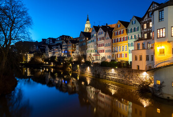 Fototapeta na wymiar “Neckarfront“ illuminated historic facades of old town of Tuebingen on Neckar River in southern Germany an a winter evening with colorful reflections, Hölderlin Tower and Church.