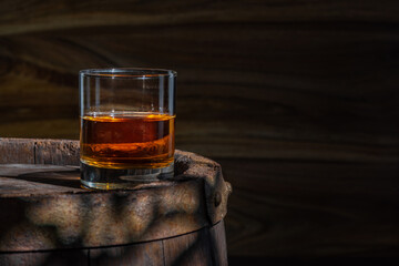 Glass decanter with whiskey, brandy on a vintage background of a rustic oaken barrel. Alcoholic beverage. Still life in the old style