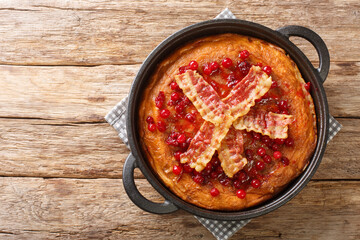 Aggakaga is a traditional South Swedish thick pancake with fried bacon and lingonberries closeup in the pan on the wooden table. Horizontal top view from above