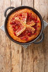 Aggakaka Egg cake is a traditional Scanian dish served with fried slices of pork belly and lingon berries closeup in the pan on the wooden table. Vertical top view from above