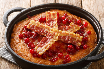 Aggakaga is a traditional South Swedish thick pancake with fried bacon and lingonberries closeup in the pan on the wooden table. Horizontal